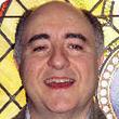 A man smiling in front of a stained glass window.