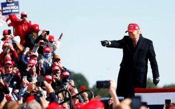 Donald Trump in a red hat waves at a crowd in red hats.