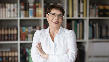 A professor stands smiling in front of a bookcase